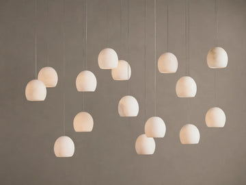 Arica Linear Chandelier with multiple glowing, spherical alabaster shades hanging at varying heights against a warm neutral wall.
