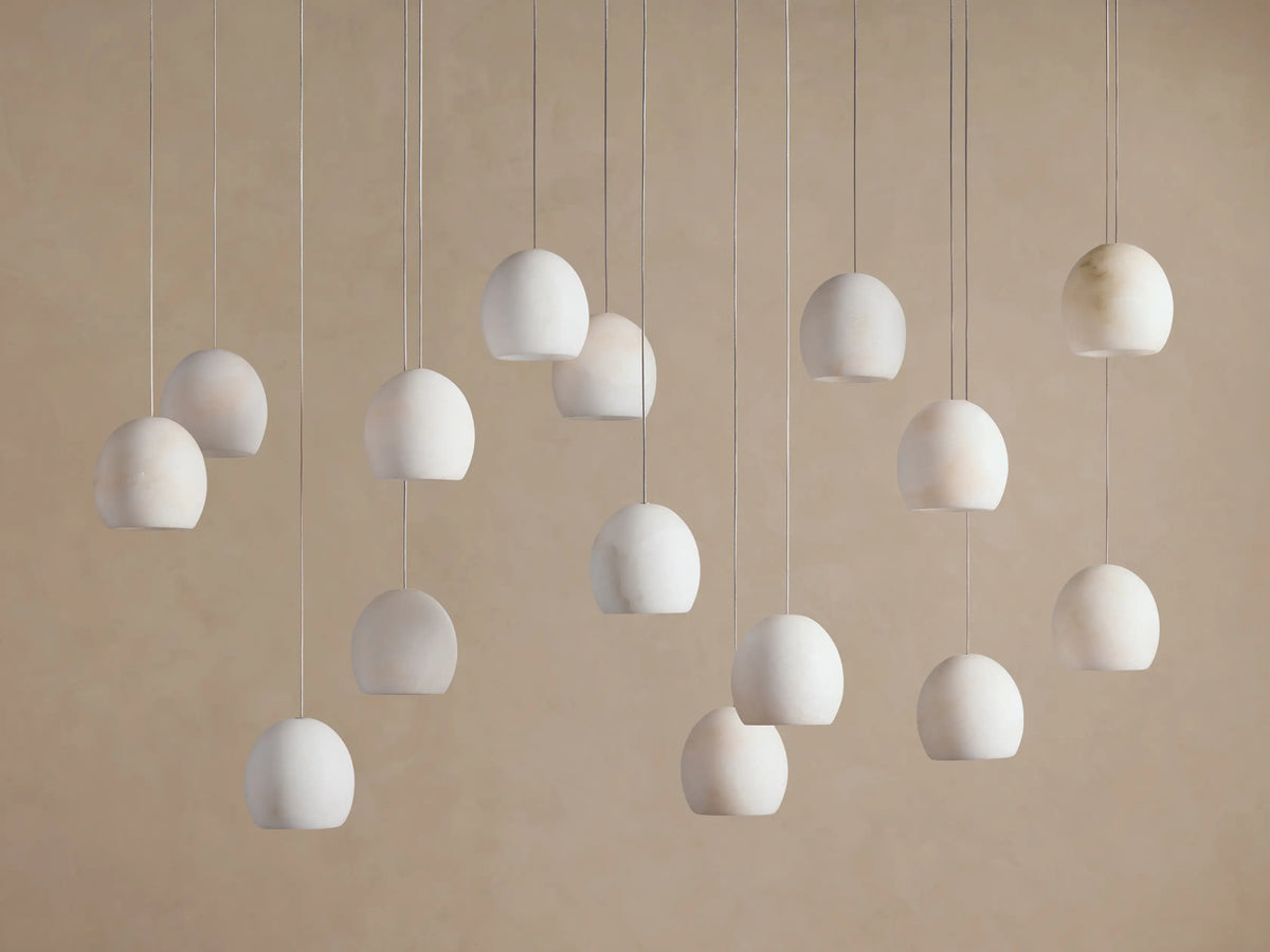 Arica Linear Chandelier with multiple glowing, spherical alabaster shades hanging at varying heights against a warm neutral wall.