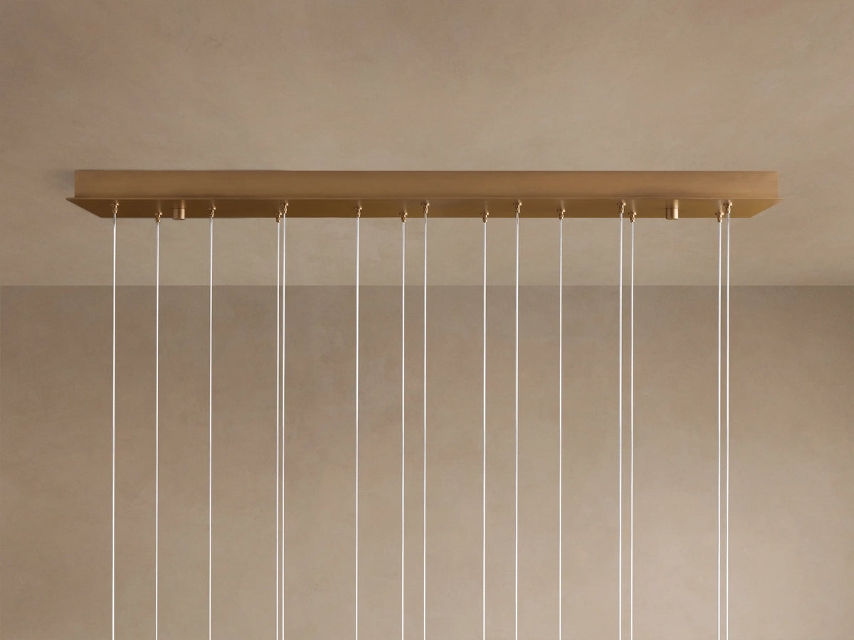 Multiple spherical, translucent alabaster shades of the Arica Linear Chandelier glow softly, suspended by thin silver cables.
