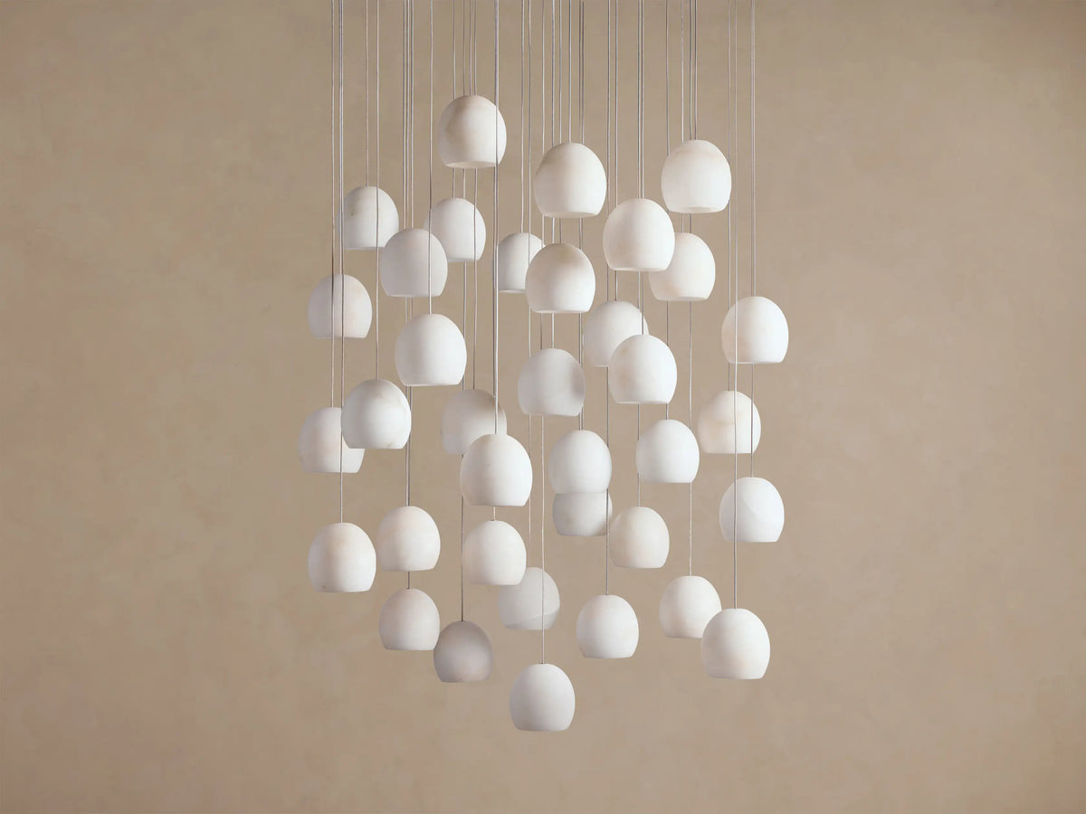 Arica Round Chandelier with numerous white, round alabaster shades suspended at varying heights against a light beige wall.