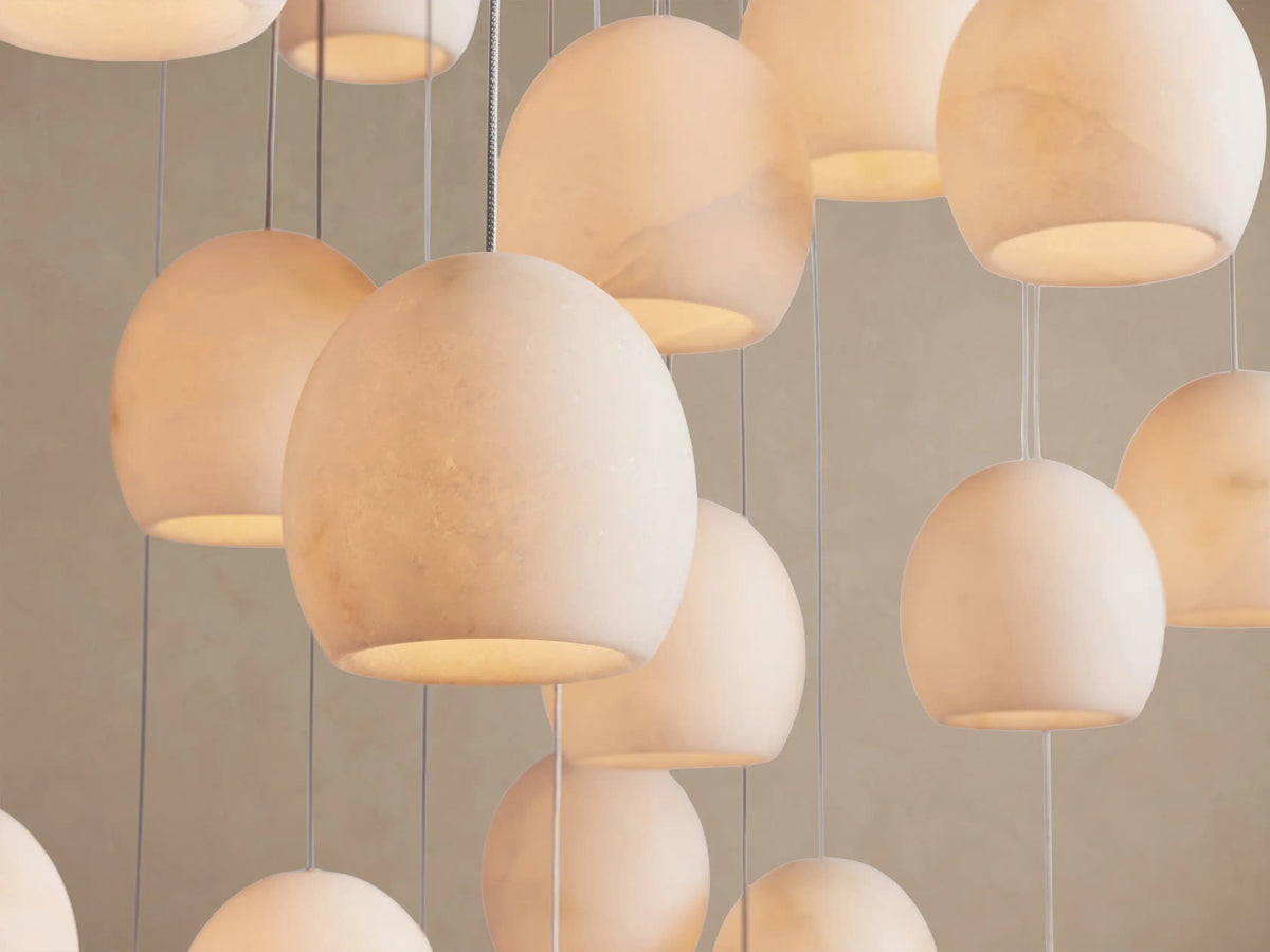 Arica Round Chandelier with multiple glowing, round alabaster stone shades suspended by thin cables against a light background.