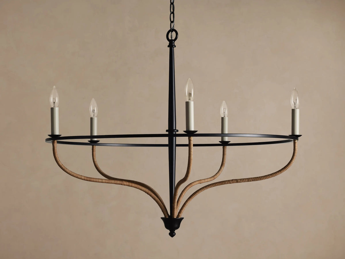 Black iron Rosalind chandelier with five illuminated candle-like bulbs. Curved arms are wrapped in natural rattan.