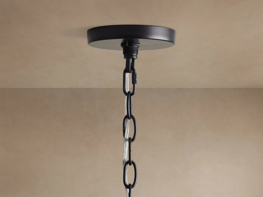 Close-up of Rosalind Rattan Chandelier in Black. Matte black iron frame, a rattan-wrapped arm, and a lit candelabra bulb.