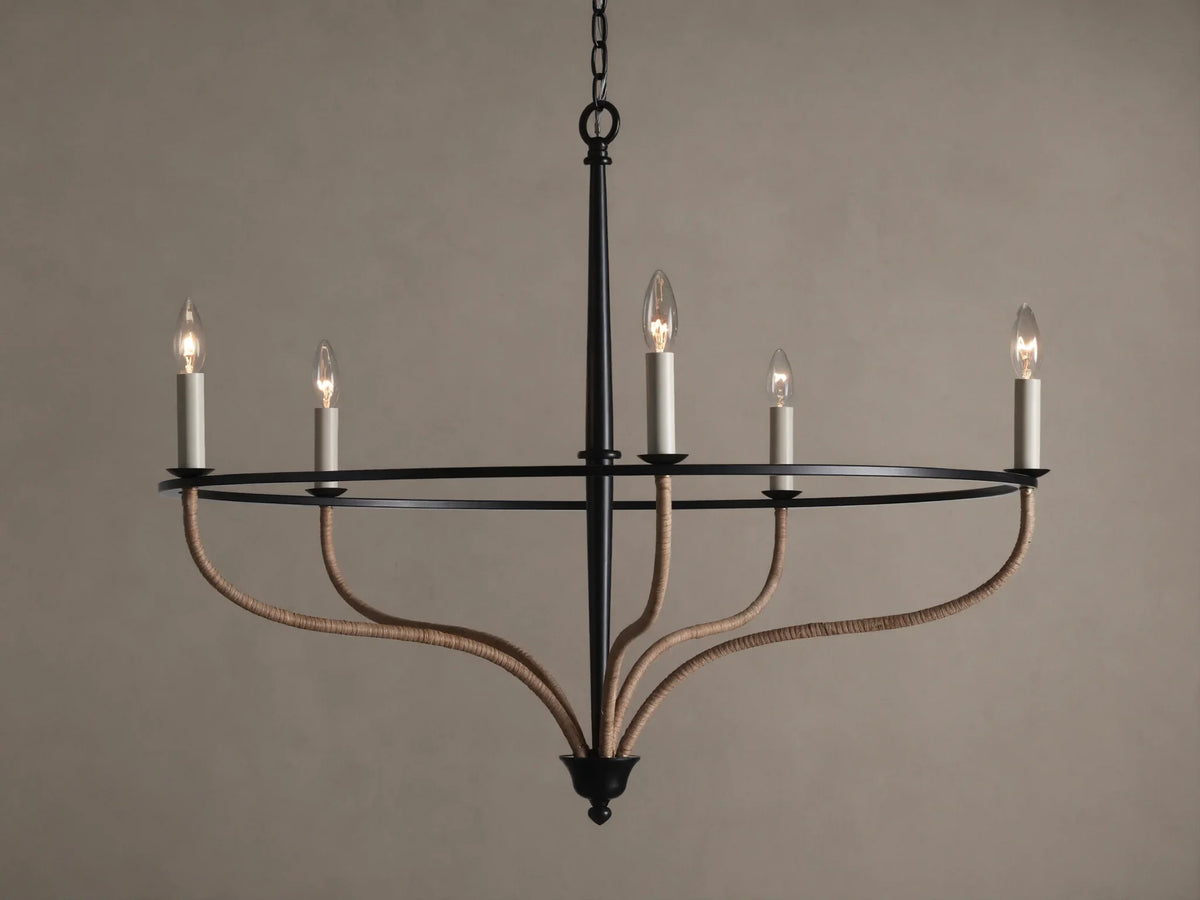 Black iron Rosalind chandelier with five illuminated candle-like bulbs. Curved arms are wrapped in natural rattan.