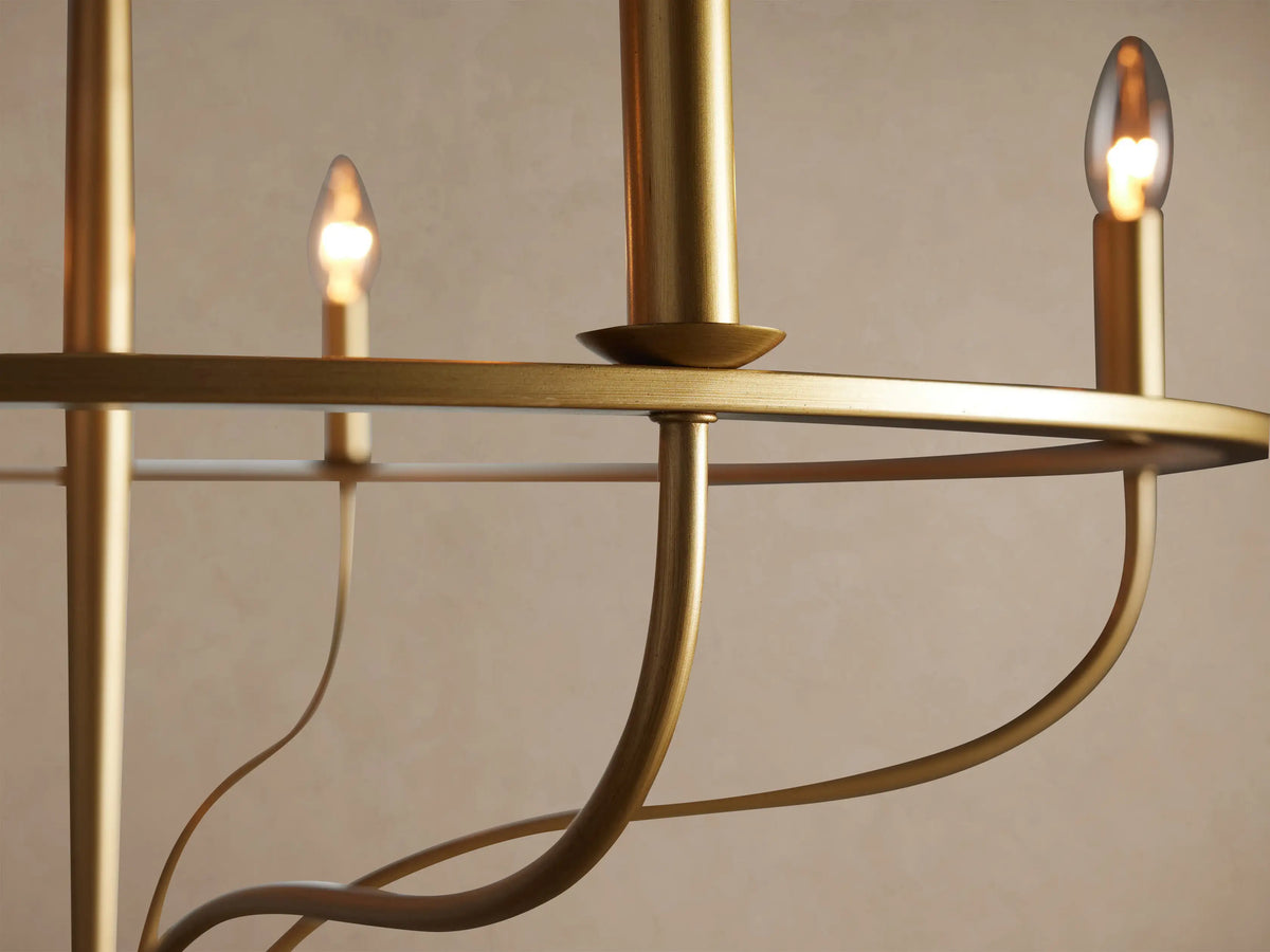 Rosalind Chandelier: Brass-finished iron, circular frame with 5 unlit candle-style bulbs, hanging against a plain wall.