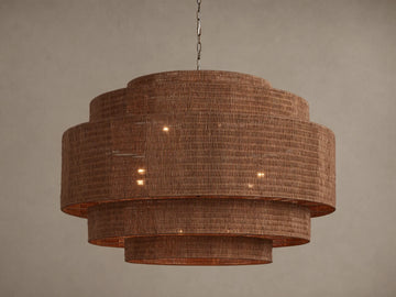 Paloma 52" tiered brown woven rattan chandelier hangs from a chain, with warm light glowing from within its shades.
