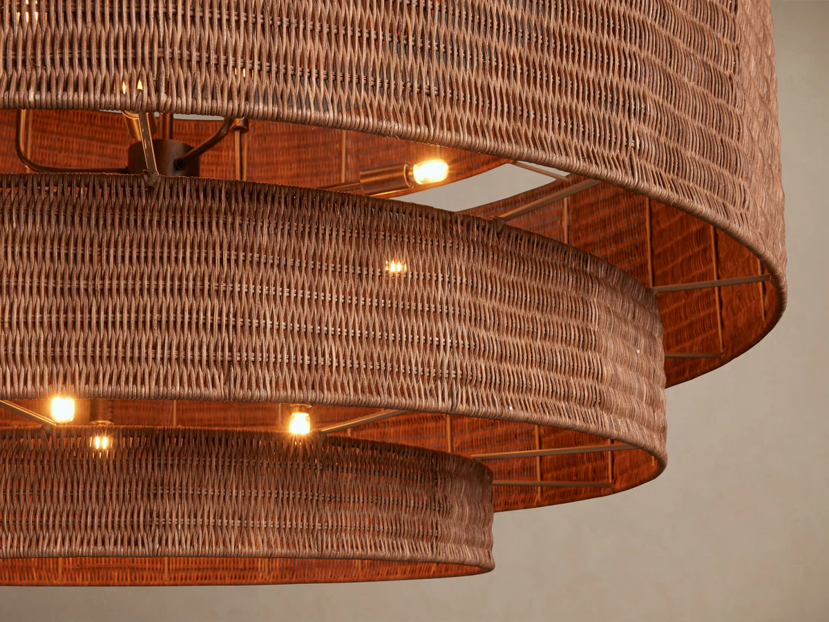 Paloma 52" Chandelier, a large tiered warm brown woven rattan chandelier suspended from a silver chain against a tan wall.