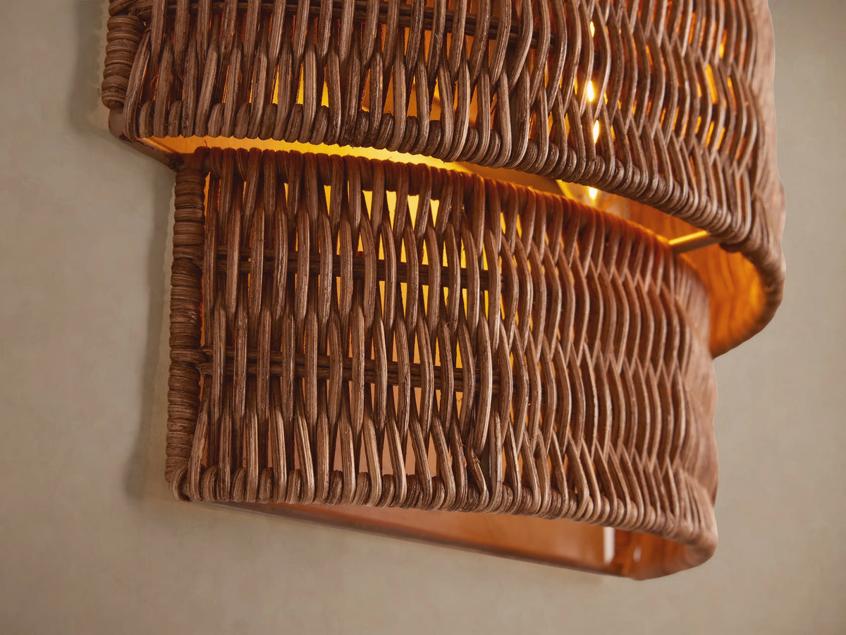 Paloma Sconce: Curved, layered design, handwoven natural tan rattan shade mounted vertically on a plain light brown wall.