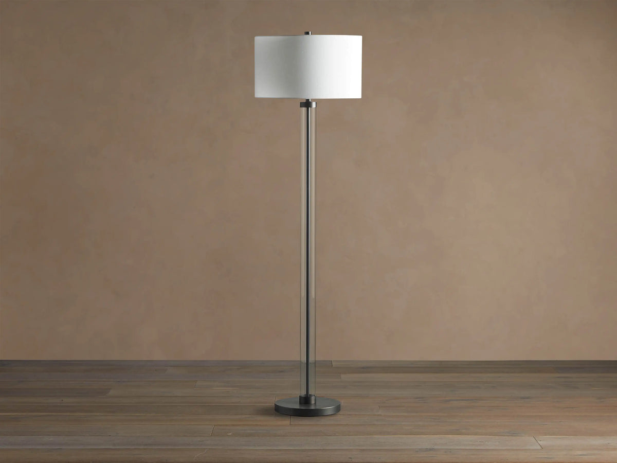 Glass Column Floor Lamp with a tall, clear glass column, dark metal base & top, and a white cylindrical linen shade.