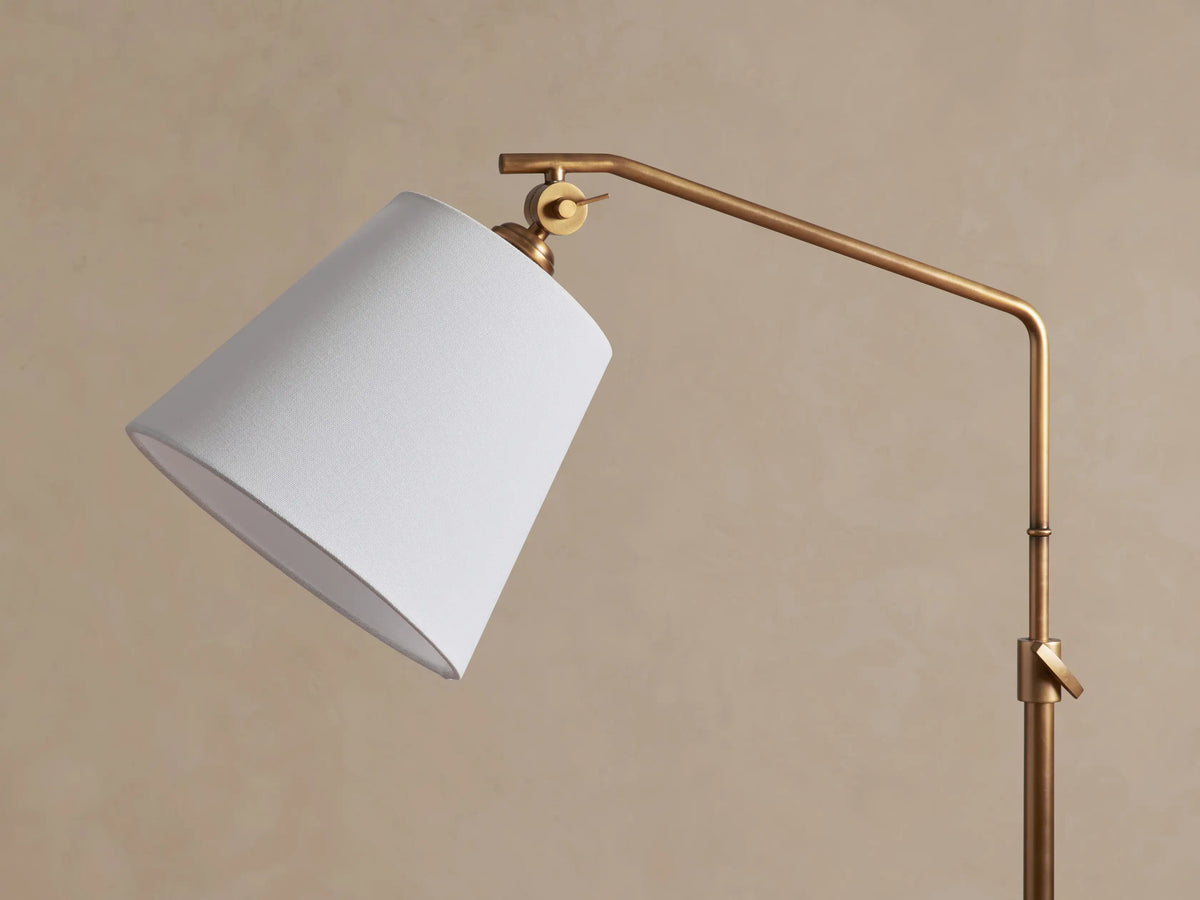 Kellen Floor Lamp: aged-brass, adjustable arm, angled white linen shade, round base, clear cord with foot switch on wood floor.