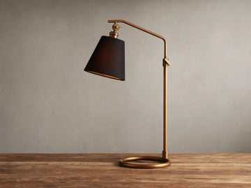 Kellen Antiqued Brass Table Lamp with dark tapered linen shade on adjustable brass stand, placed on wooden surface.