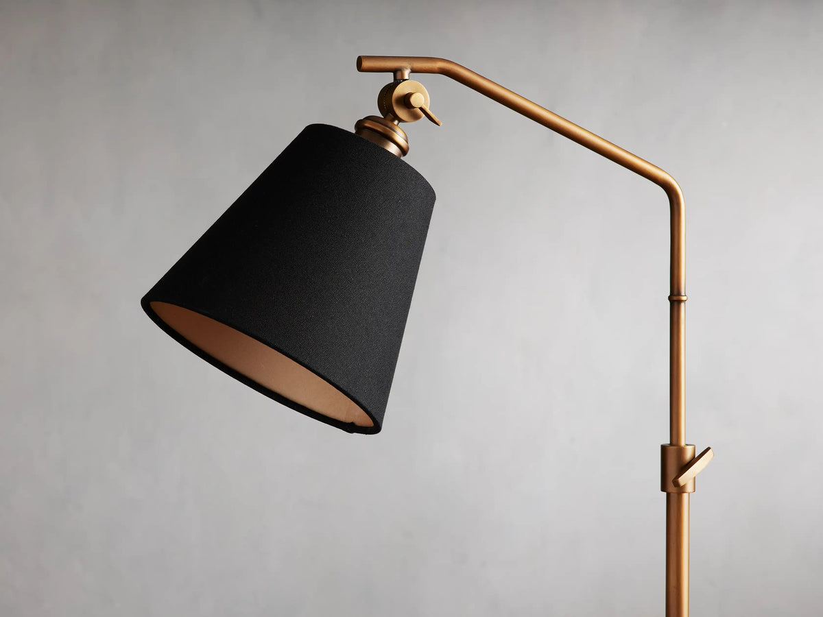 Kellen Antiqued Brass Table Lamp with adjustable height, black linen shade, and brass arm on a wooden surface.