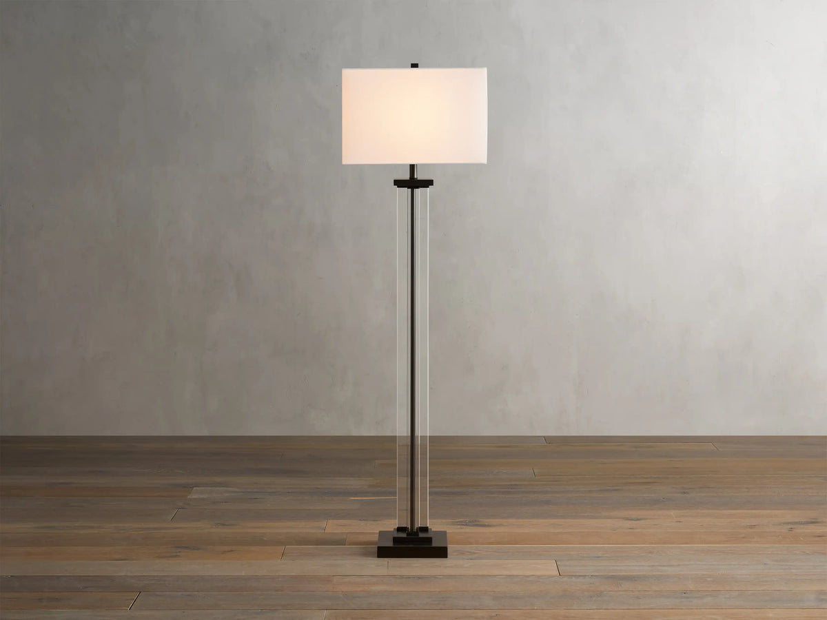 Dawson Floor Lamp with rectangular white shade, clear crystal and iron stand, on wooden floor, against a light gray wall.