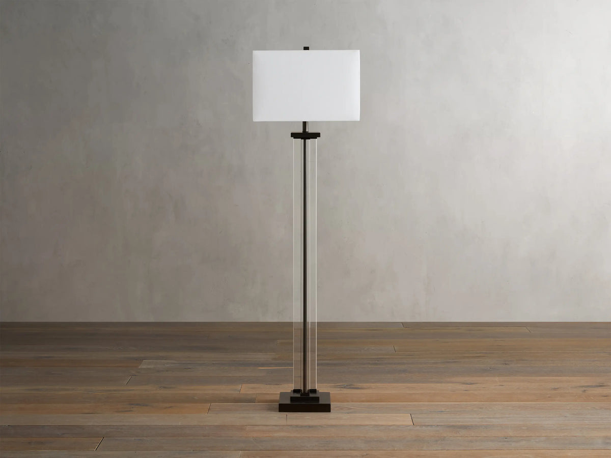 Dawson Floor Lamp with rectangular white shade, clear crystal and iron stand, on wooden floor, against a light gray wall.