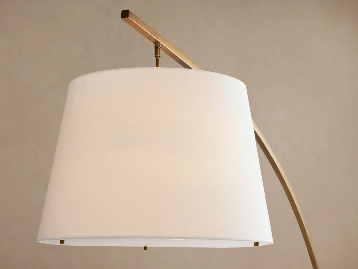 Tadeo arc floor lamp with a brass-finished pole, white linen shade, and rectangular white Carrara marble base on a wood floor.