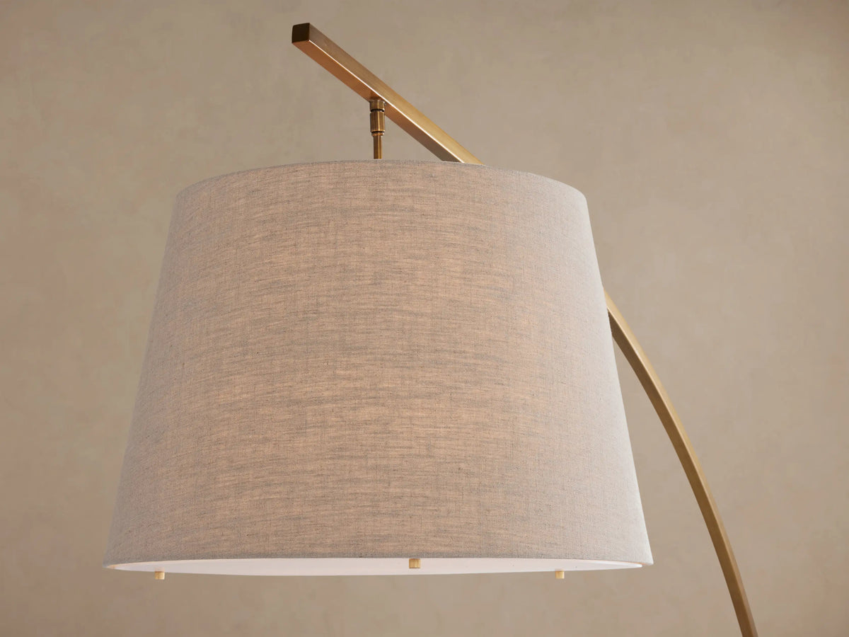 Tadeo Floor Lamp: arched brass-finish iron stand, white marble base, light beige linen drum shade, on a wooden floor.