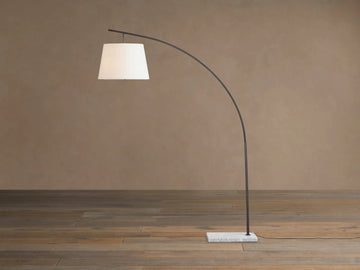 Tadeo Floor Lamp with a curved dark bronze arm, white linen shade, and rectangular white marble base on a wood floor.