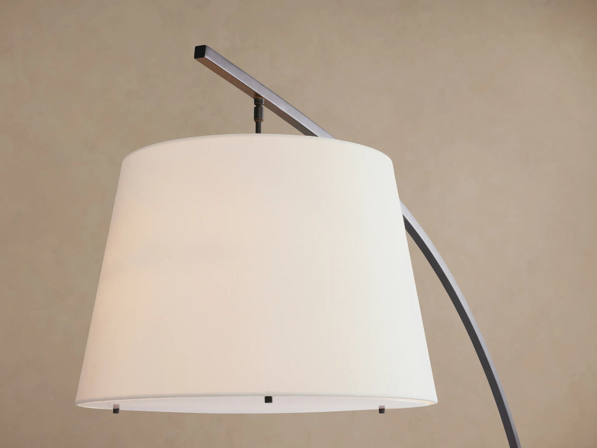 Tadeo Floor Lamp with an arched dark bronze stand, white linen shade, and rectangular Carrara marble base on a wood floor.