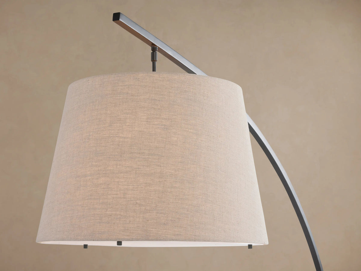 Tadeo arc floor lamp with dark bronze arm, light linen shade, and rectangular white marble base on a wooden floor.