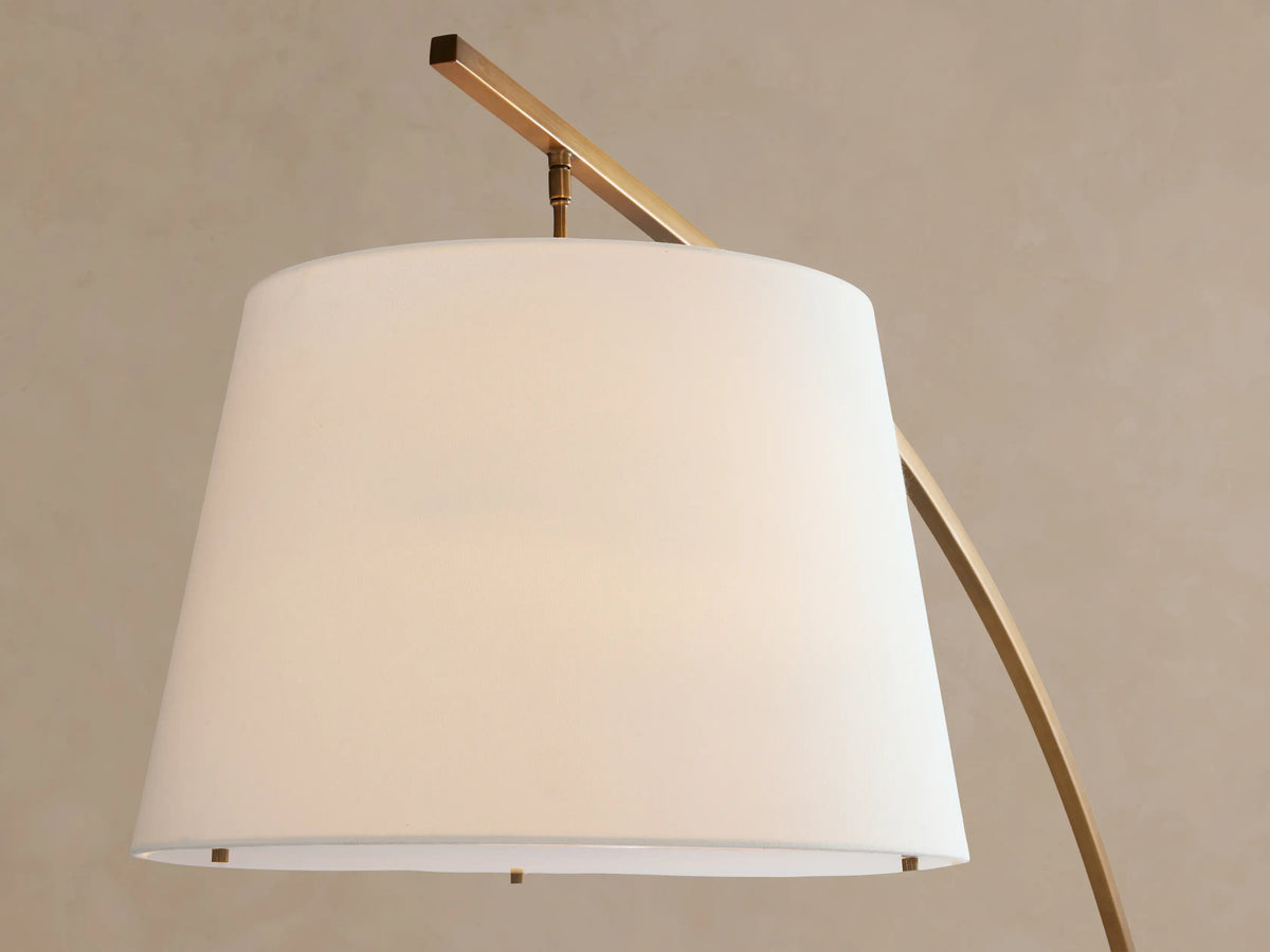 Tadeo Floor Lamp: stylish arched brass floor lamp with a white linen shade and a dark marble base, on a wooden floor.