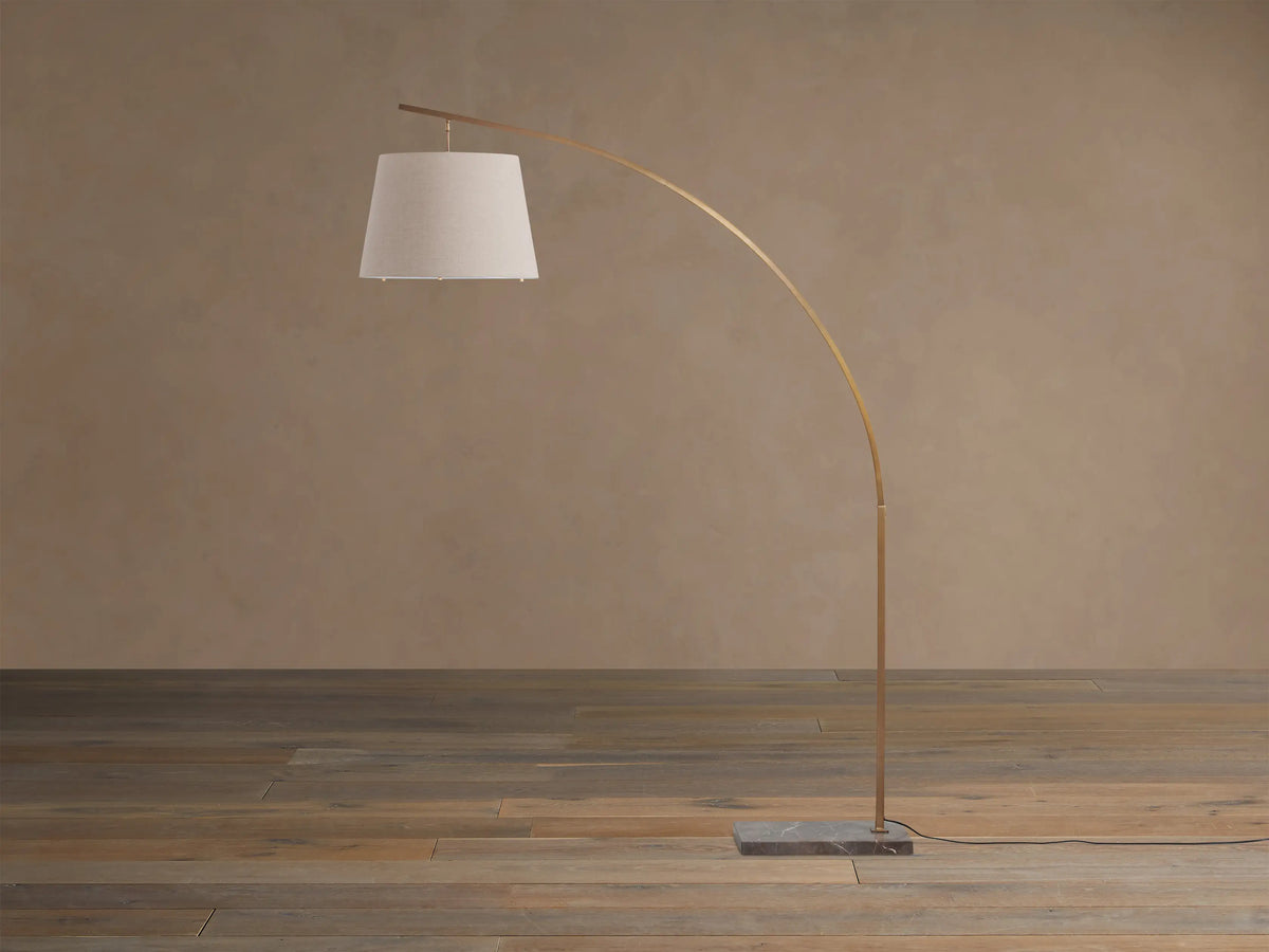 Tadeo Floor Lamp: Arched brass-finished stand, natural linen shade, and espresso marble base on a wooden floor.