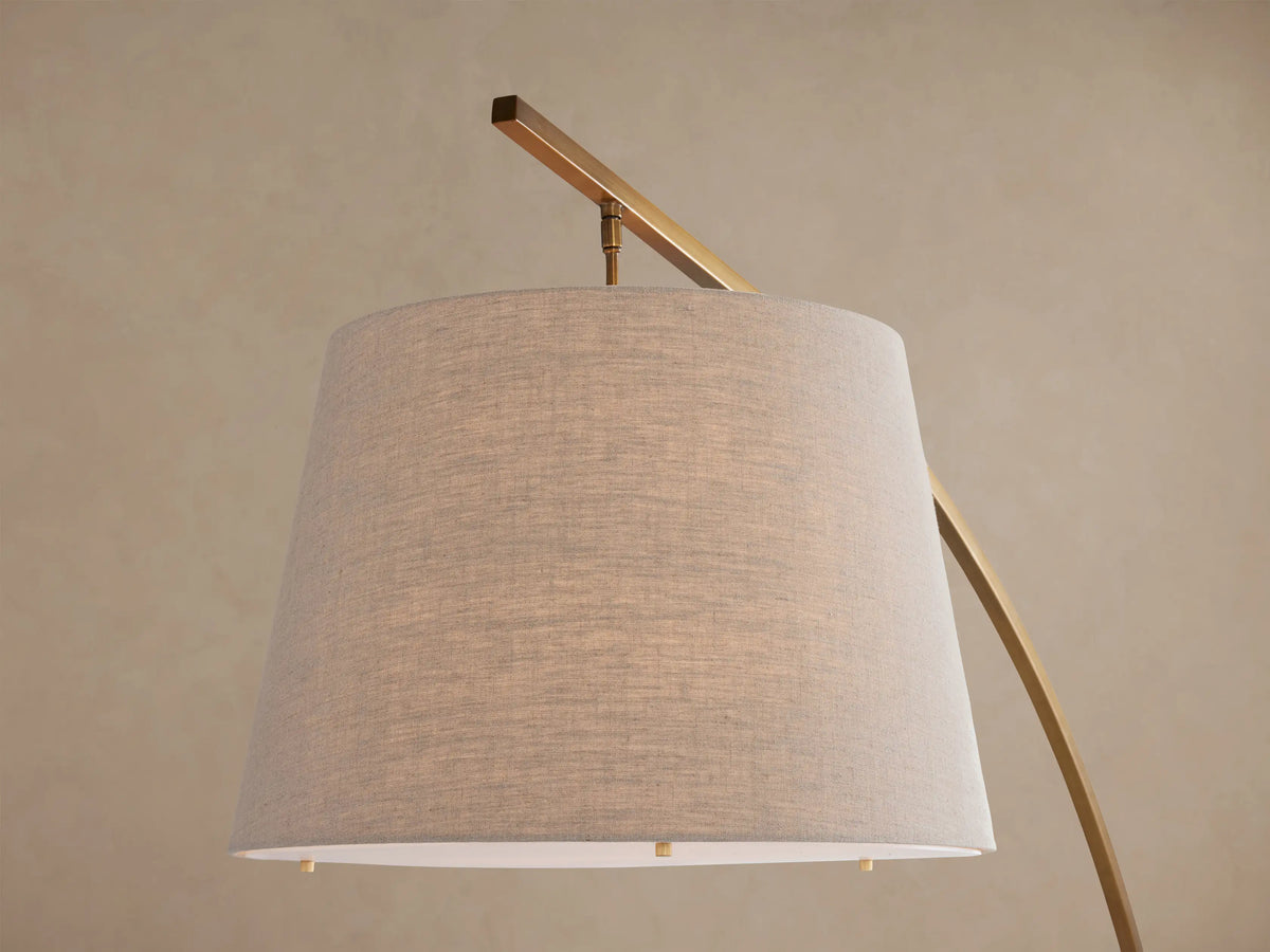 Tadeo Floor Lamp: arched brass frame, light beige linen shade, and dark espresso marble base on a wooden floor.