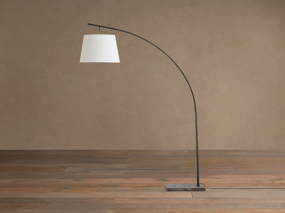 Tadeo Floor Lamp: A dark bronze arc lamp with a white linen drum shade and square espresso marble base on a wood floor.