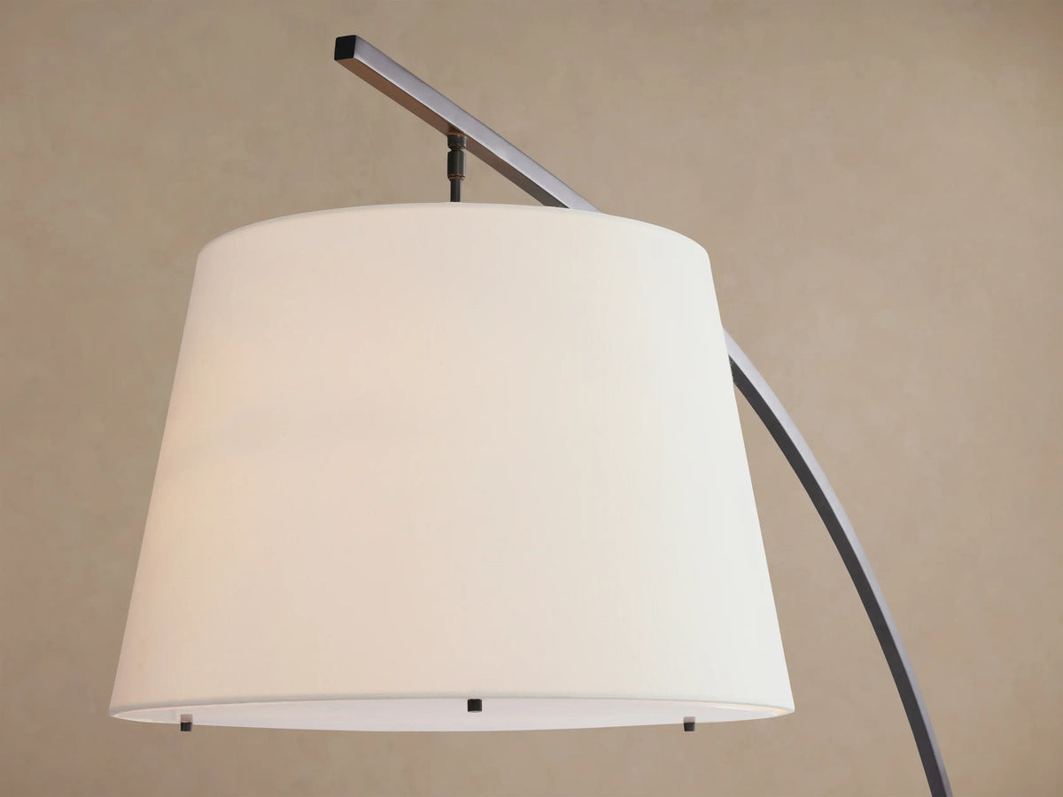 Tadeo Floor Lamp with dark arched stand, white linen shade, and dark espresso marble base, on wood floor.