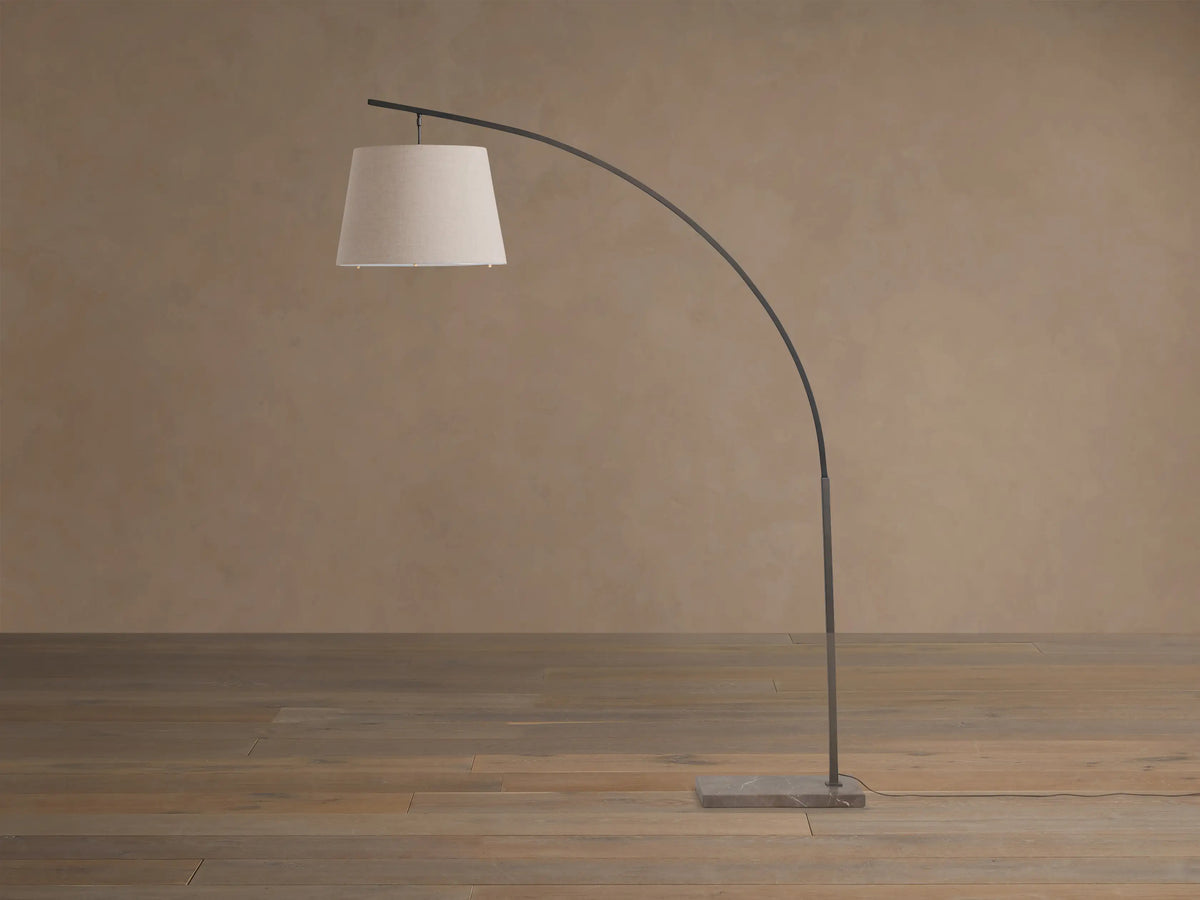 Tadeo Floor Lamp with dark arched iron stand, light linen shade, and rectangular espresso marble base on wood floor.
