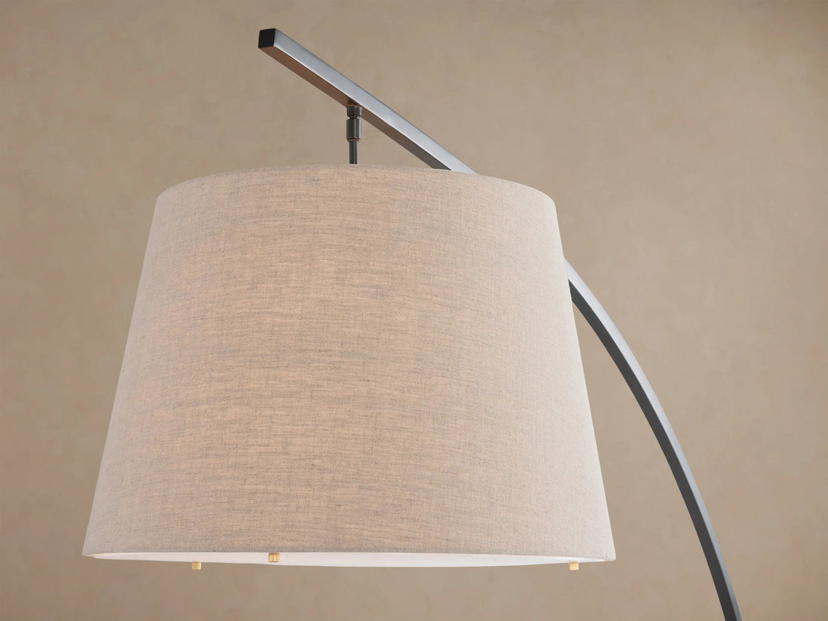 Tadeo Floor Lamp with an arched dark bronze arm, light linen shade, and rectangular espresso marble base, standing on a wood floor.