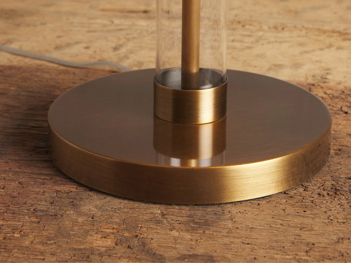 Glass Column Table Lamp with clear glass column, white linen shade, and gold base on a rustic wood table.