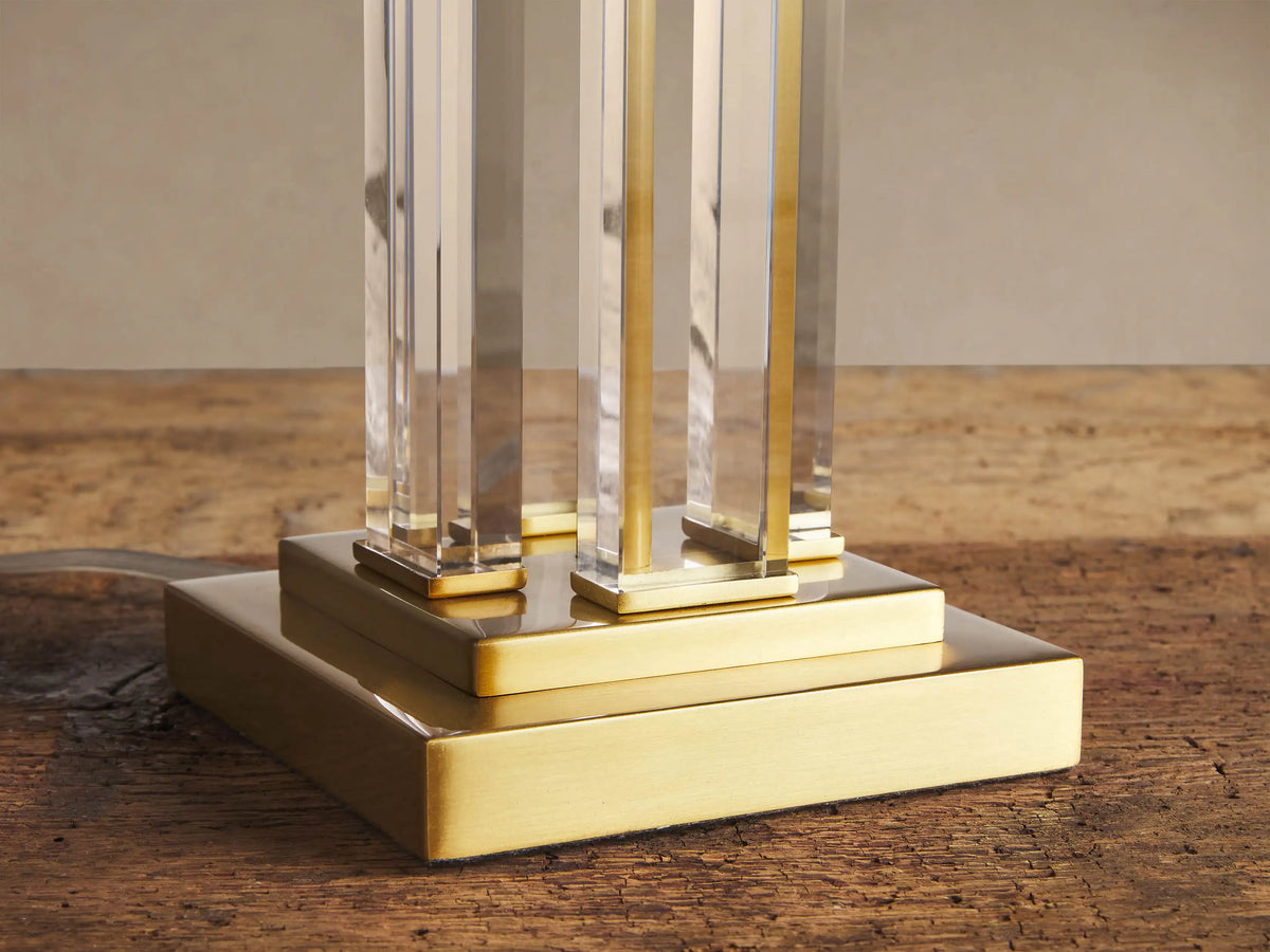 Dawson Table Lamp with rectangular white shade, gold and clear acrylic uprights, and a square gold base on a wood surface.