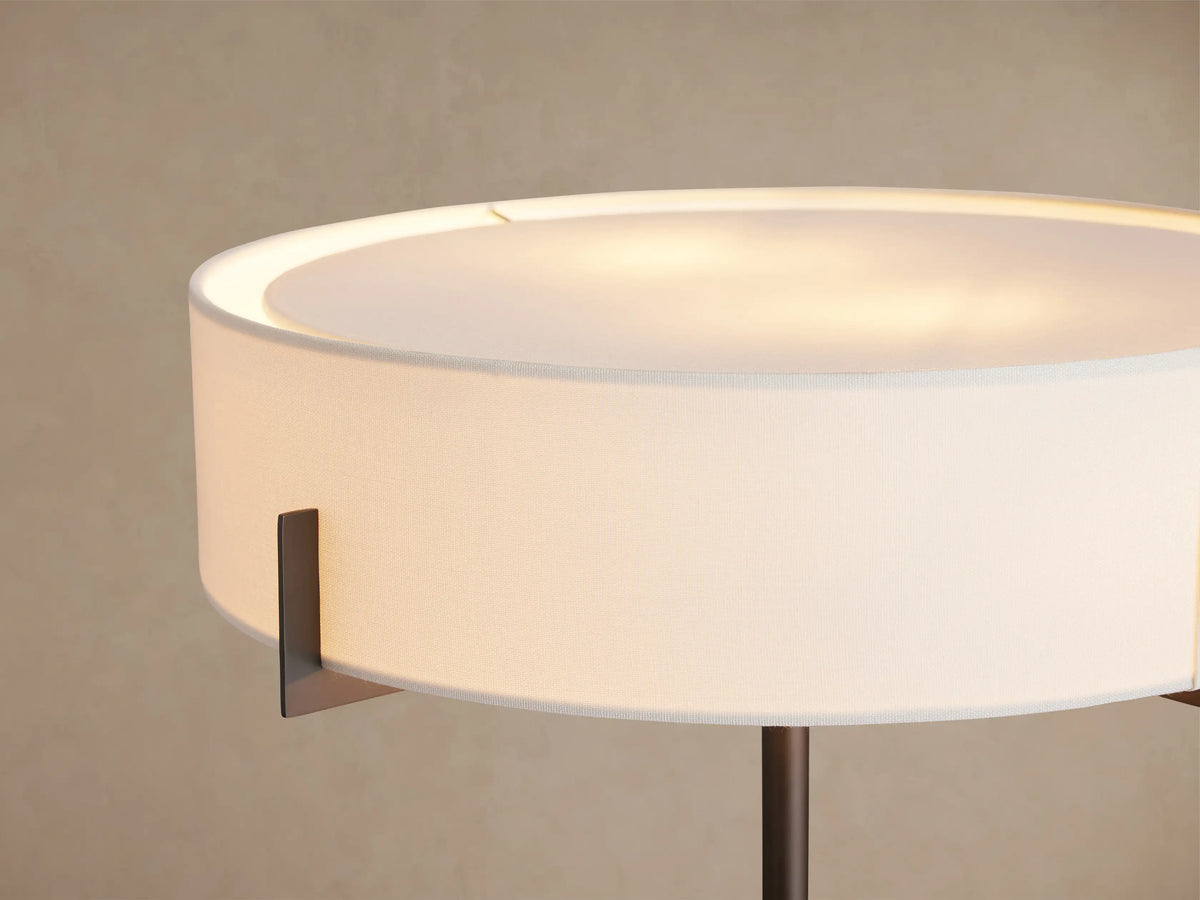 Frederic Table Lamp: bronze iron frame, white linen drum shade, cream marble base on dark square. On wood table.