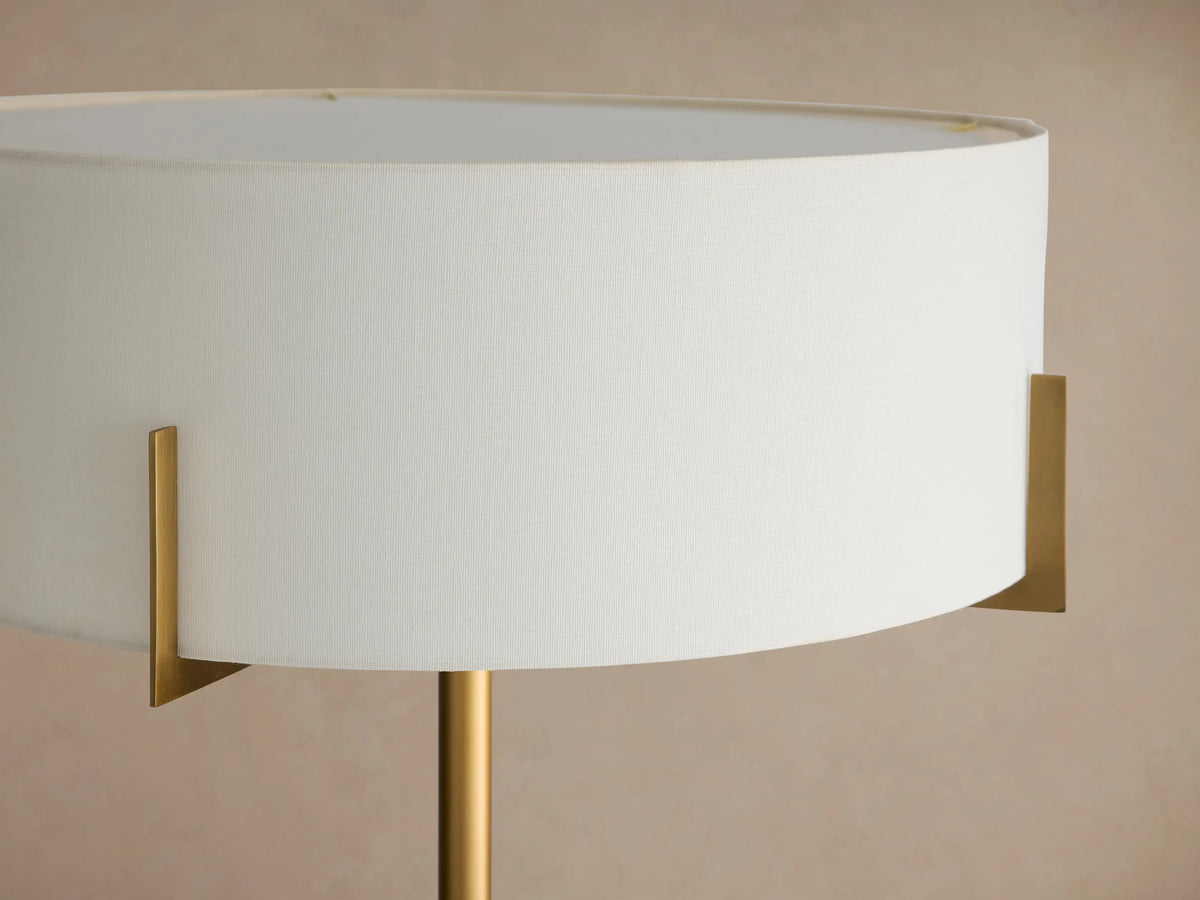 Frederic Floor Lamp: antiqued brass iron pole, white linen shade, and black granite base, standing on a wooden floor.