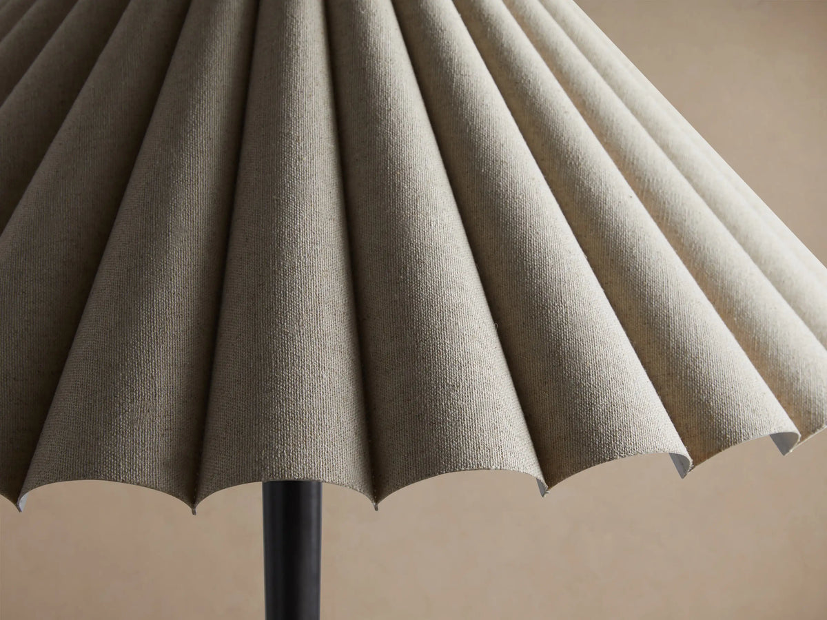 Santiago Table Lamp with pleated natural linen shade and dark bronze-finished cast iron base on a wooden surface.