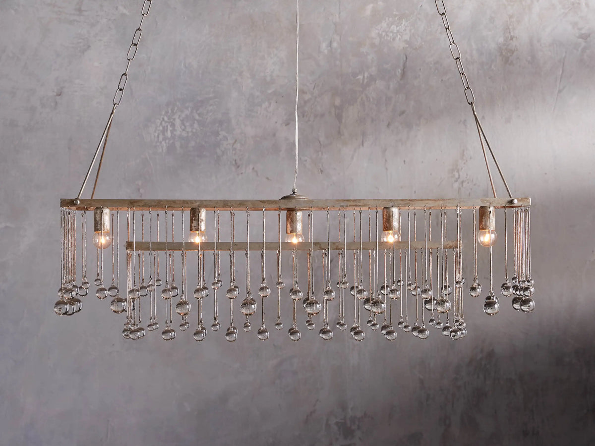 Aubrey Rectangular Chandelier with a silver handcrafted iron frame, hanging Italian glass crystals, and five glowing bulbs.