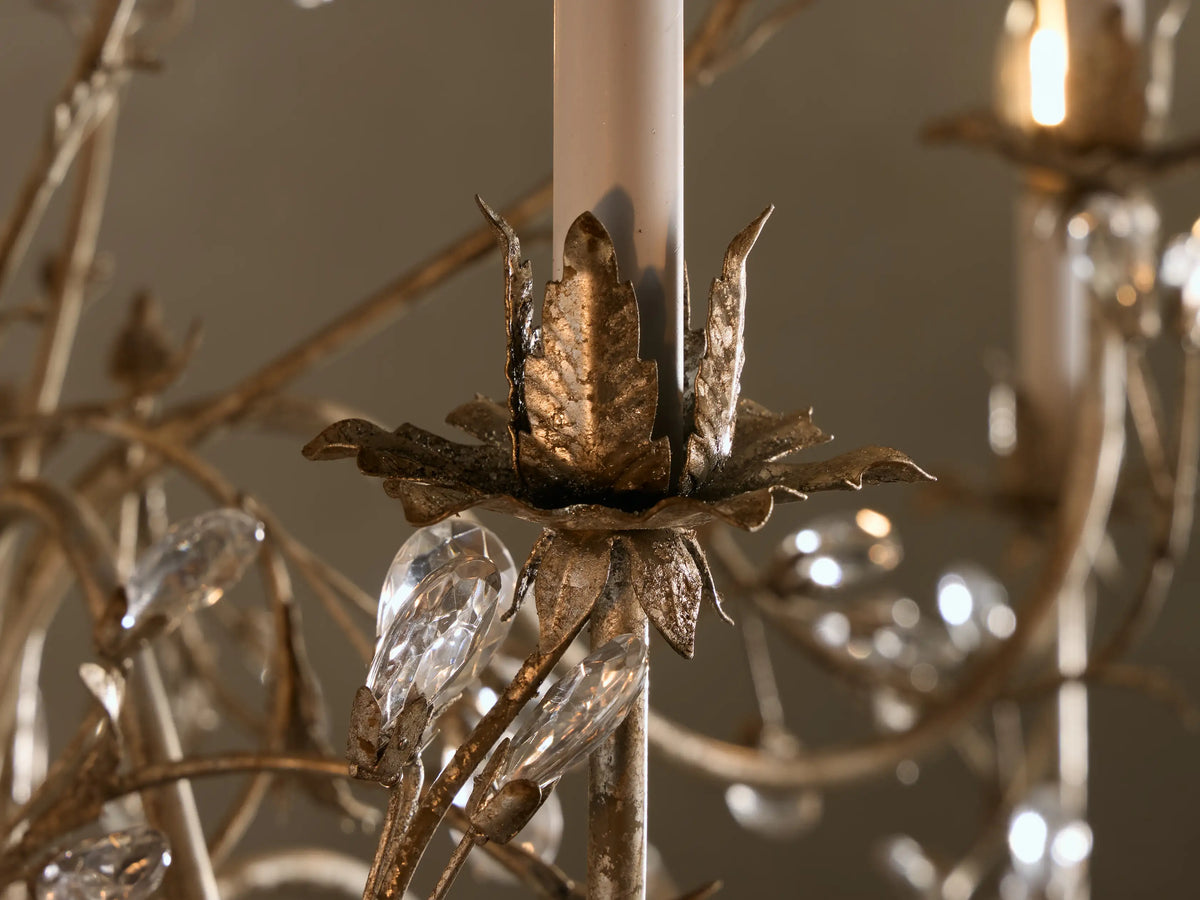Close-up of Claudette Chandelier, grey lacquered iron frame with silver leaf, intricate branches, clear glass crystals, warm candle bulbs.