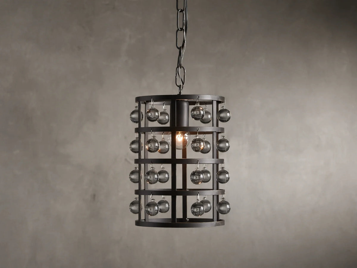 Iron cage pendant with antiqued metallic finish, adorned with Italian crystal spheres, hanging from a chain on a textured wall background.