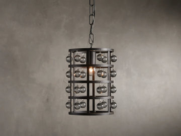 Iron cage pendant with antiqued metallic finish, adorned with Italian crystal spheres, hanging from a chain on a textured wall background.