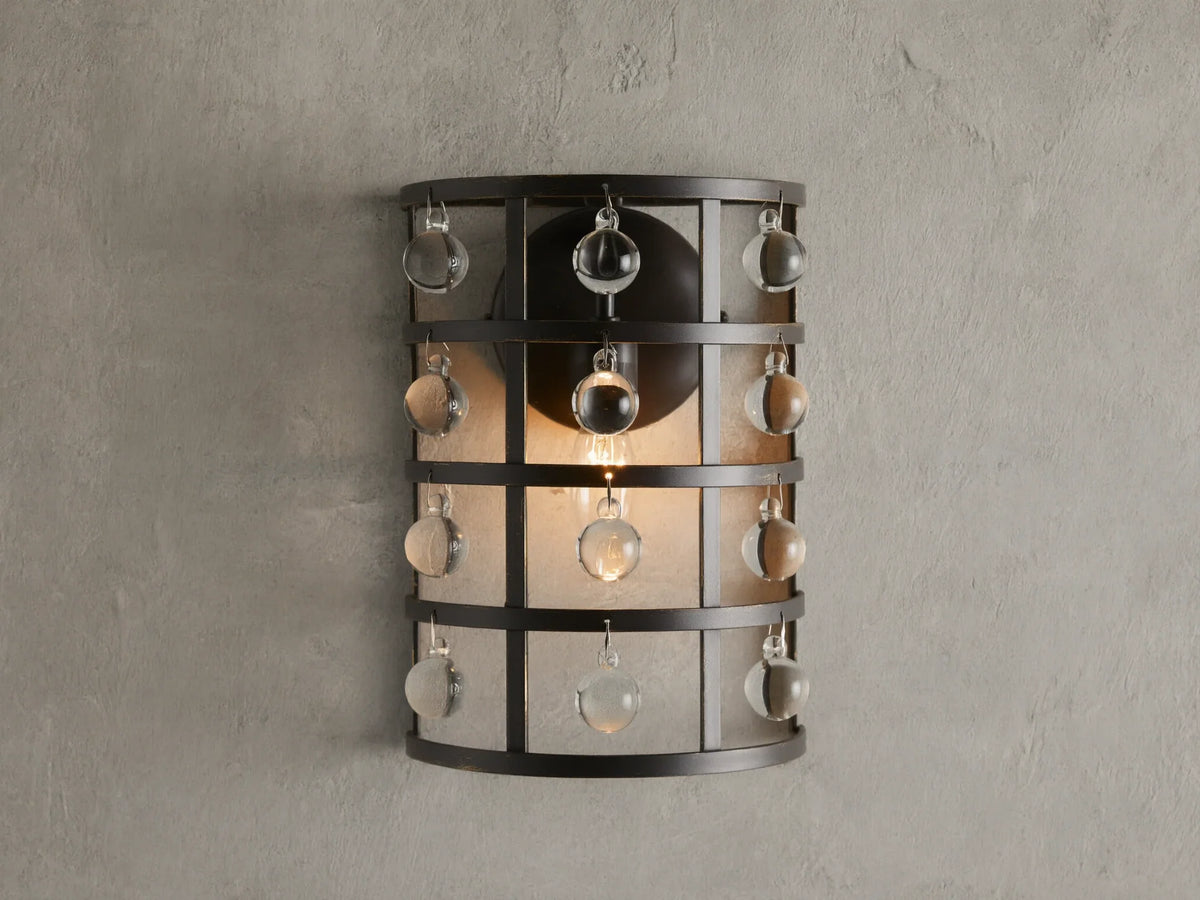 Iron cage sconce with antiqued metallic finish and Italian crystal spheres, mounted on a textured wall, lit from within.