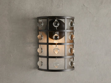 Iron cage sconce with antiqued metallic finish and Italian crystal spheres, mounted on a textured wall, lit from within.