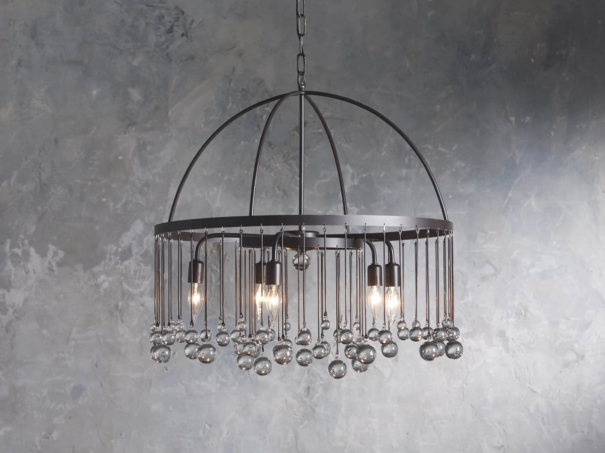 A round chandelier made of solid iron with five exposed bulbs and hanging glass accents, suspended by an iron chain.