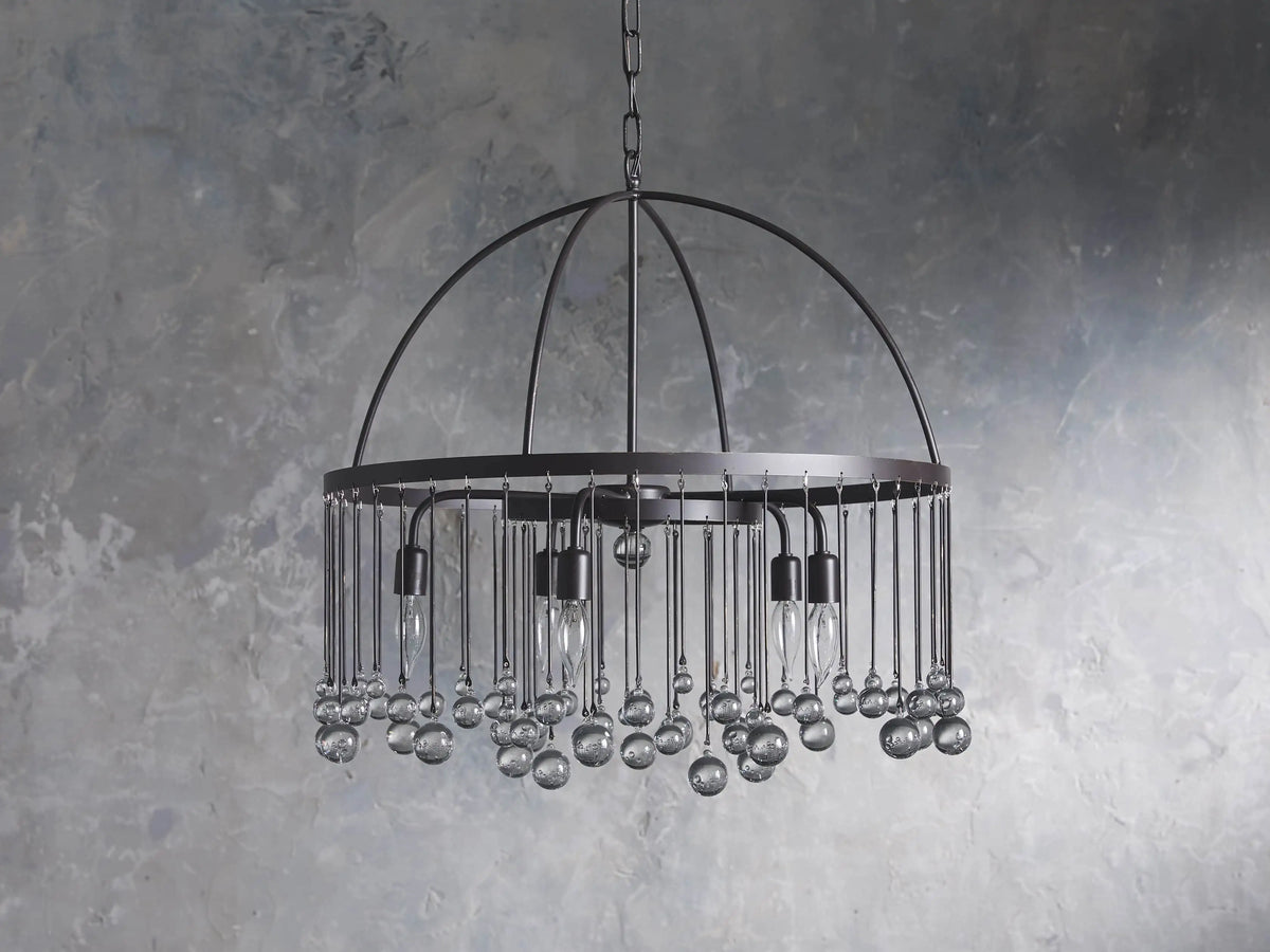 A round chandelier made of solid iron with five exposed bulbs and hanging glass accents, suspended by an iron chain.