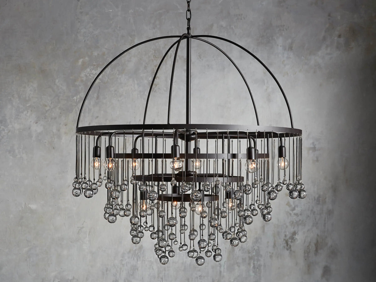 A round chandelier with a dark iron frame, featuring cascading glass orbs and five visible lit bulbs, hanging from a chain.