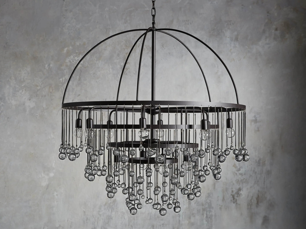 A round chandelier with a dark iron frame, featuring cascading glass orbs and five visible lit bulbs, hanging from a chain.