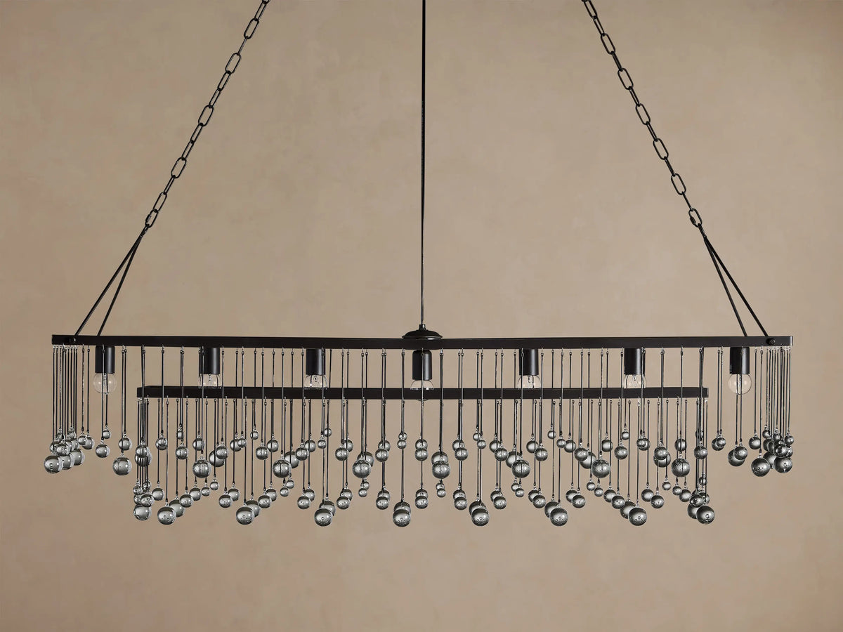 Aubrey Rectangular Chandelier: dark metal frame with 5 exposed bulbs & cascading glass spheres, hanging against a brown wall.