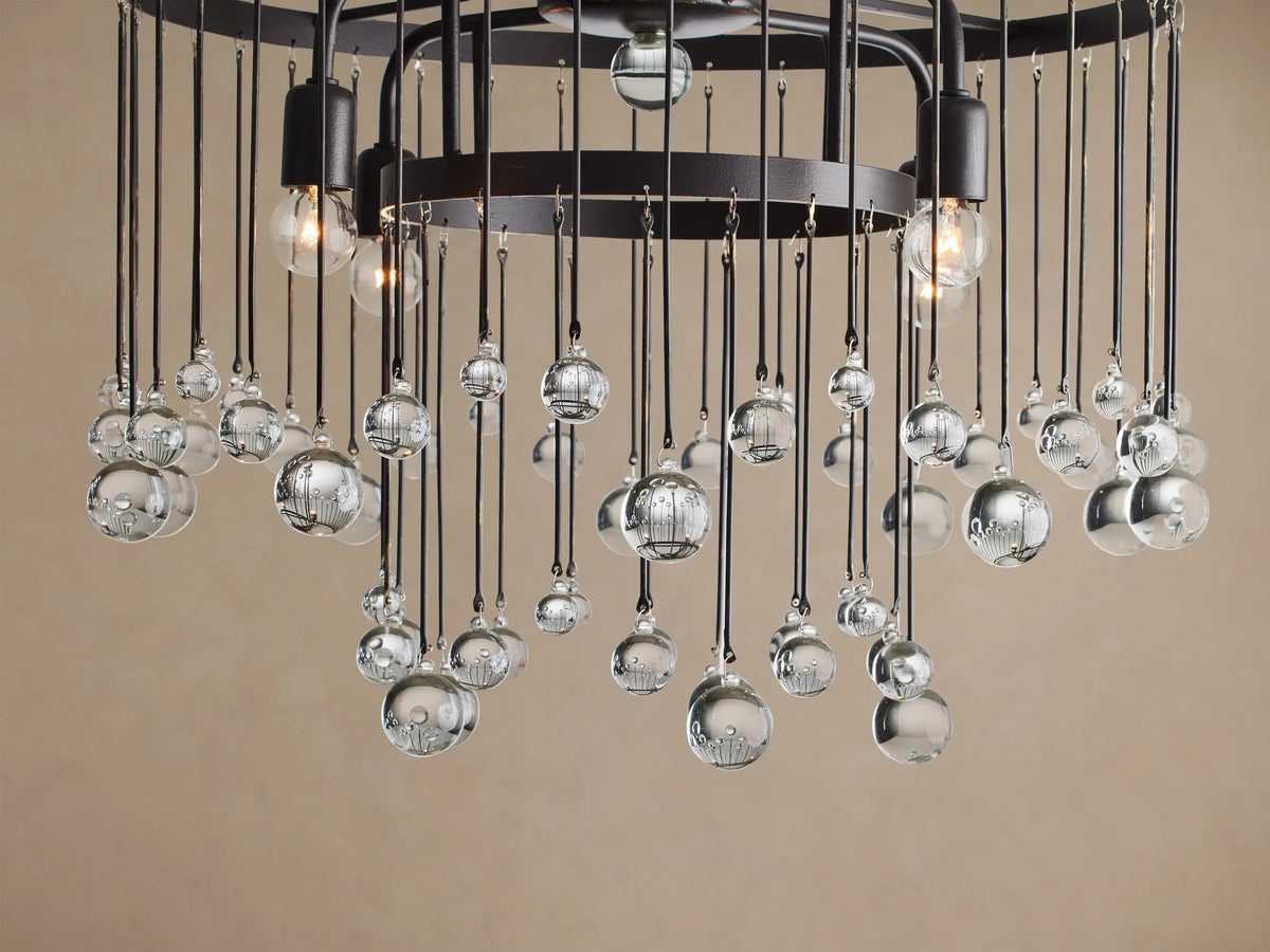Aubrey Flush Mount: Black iron frame with clear glass spheres suspended by thin rods at varying lengths, against a beige ceiling.