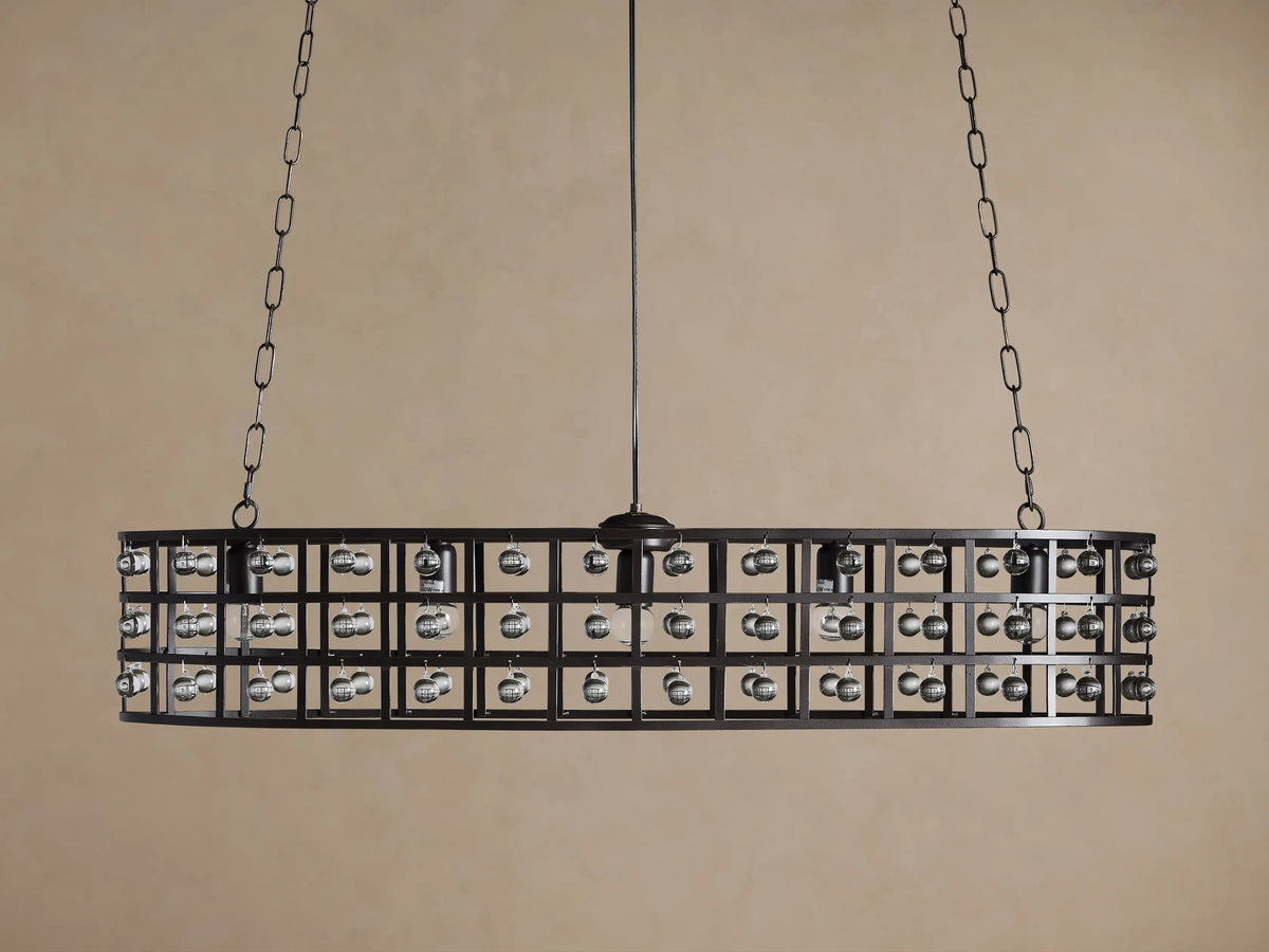 La Cage Oval Chandelier: Dark metal cage frame, oval-shaped, adorned with clear crystal spheres and glowing bulbs, suspended by chains.