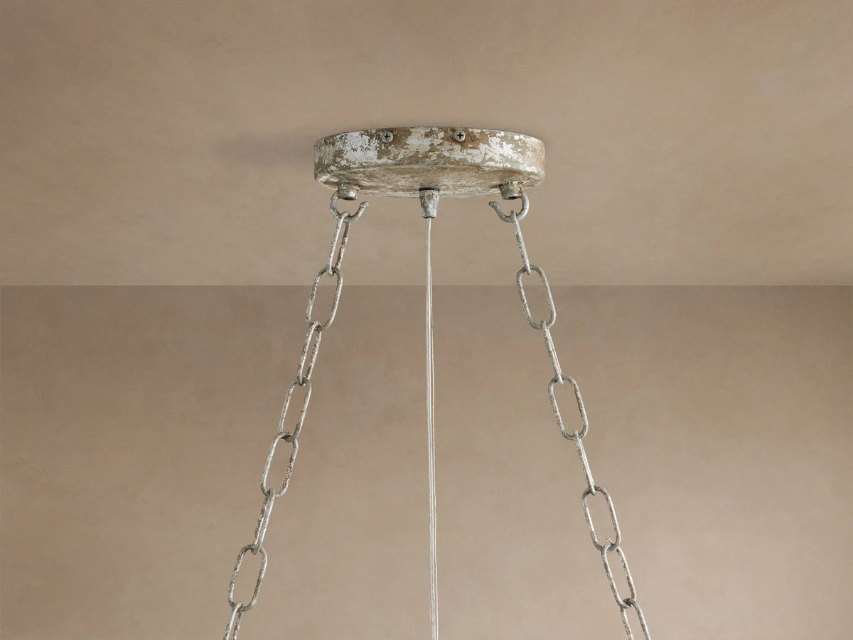 Close-up of Fiore Crown Chandelier's distressed silver/white ceiling mount with two hanging chains and a wire against a beige ceiling.