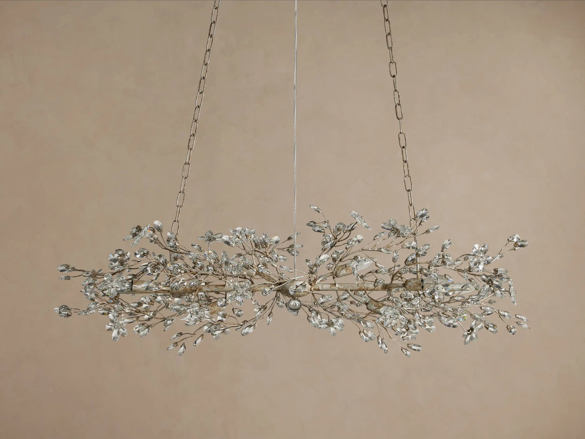 Fiore Linear Chandelier with delicate silver branches adorned with clear crystal flowers, glowing with warm light, suspended by chains.